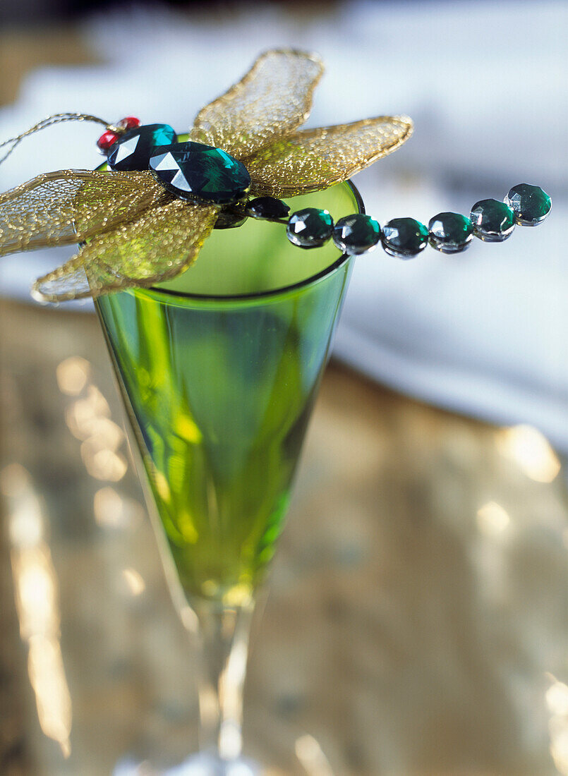 Libellen-Dekoration mit goldenen Flügeln und Halbedelsteinen auf einem grünen Glas mit Stiel
