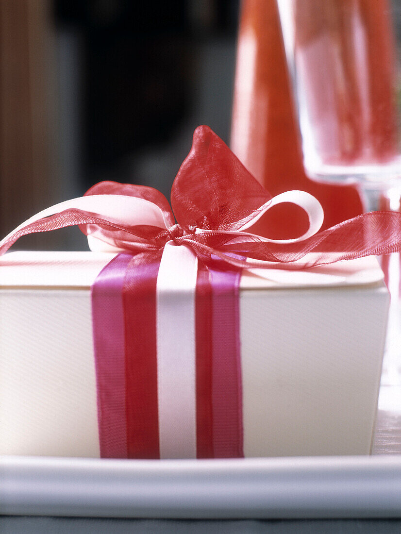 White gift box tied with pink and red ribbons on a dining table