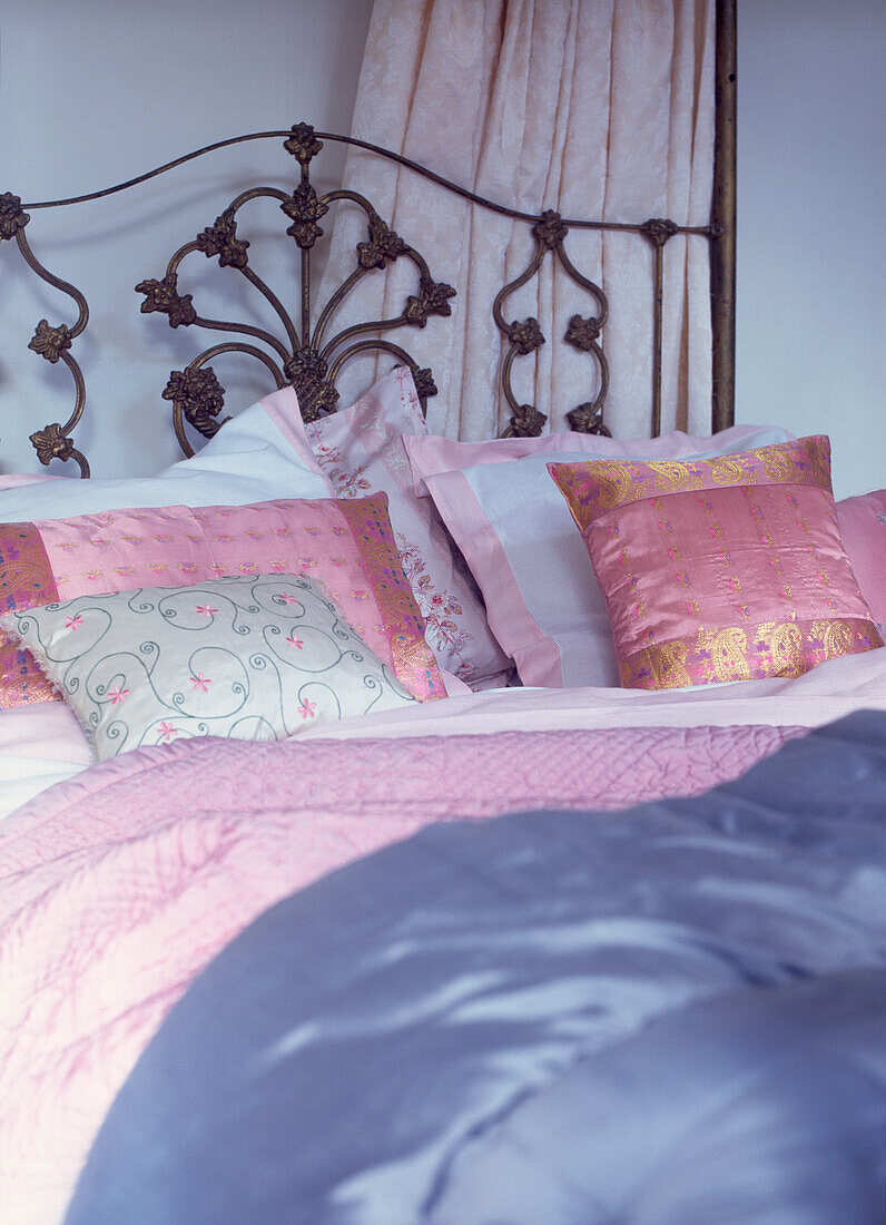 Hübsche bestickte Satinkissen und Tagesdecken auf einem dekorativen gusseisernen Doppelbett im Schlafzimmer
