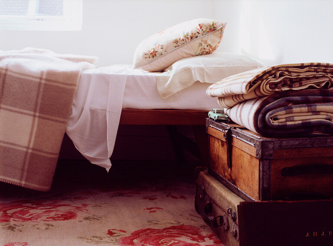 Nahaufnahme eines Ersatzbetts mit Lederkoffern auf einem hübschen blumengemusterten Teppich