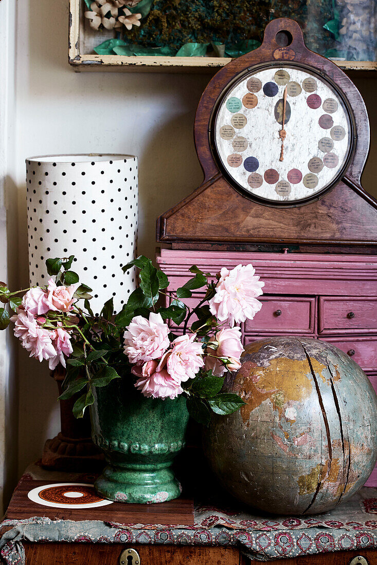 Corner detail with pink painted drawers and an antique Fortune teller and wooden globe with vase of pink roses and spotted lampshade