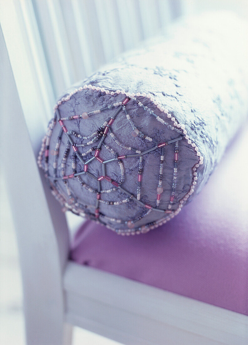 Detail of white chair with purple bolster cushion trimmed with beads