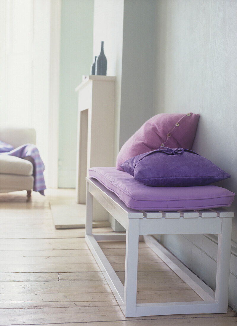 Weiße Sitzbank mit violetten Kissen in einem hellblauen Wohnzimmer