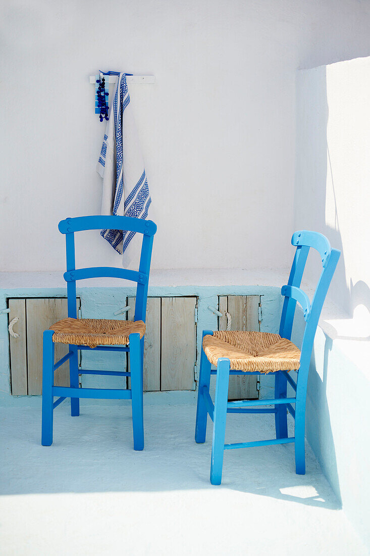 Two blue chairs in whitewashed courtyard of Greek villa