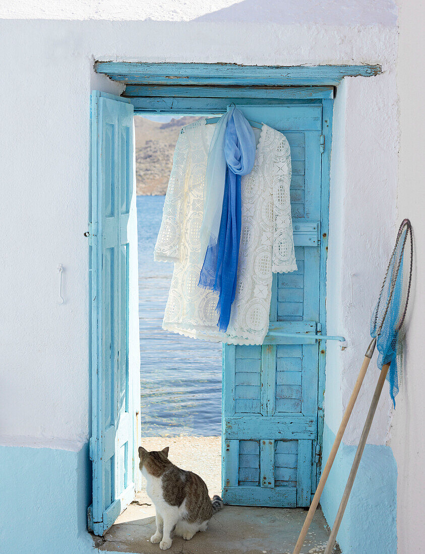Spitzenkleid hängt in der Tür einer griechischen Villa mit Fischernetz und Katze, die zurückschaut
