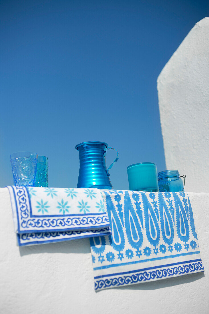 Collection of blue glassware and fabrics hang on whitewashed wall of Greek villa