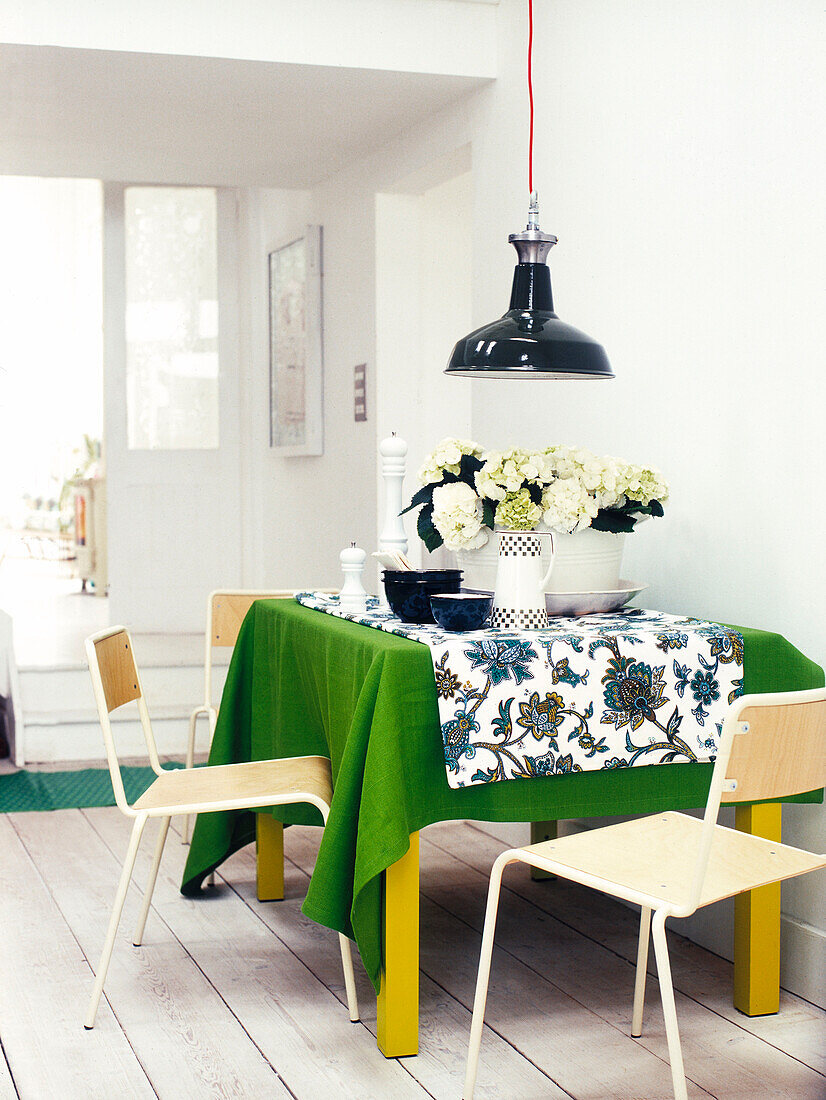Schwarze Pendelleuchte über dem Esstisch mit Blumen und grünem Tuch