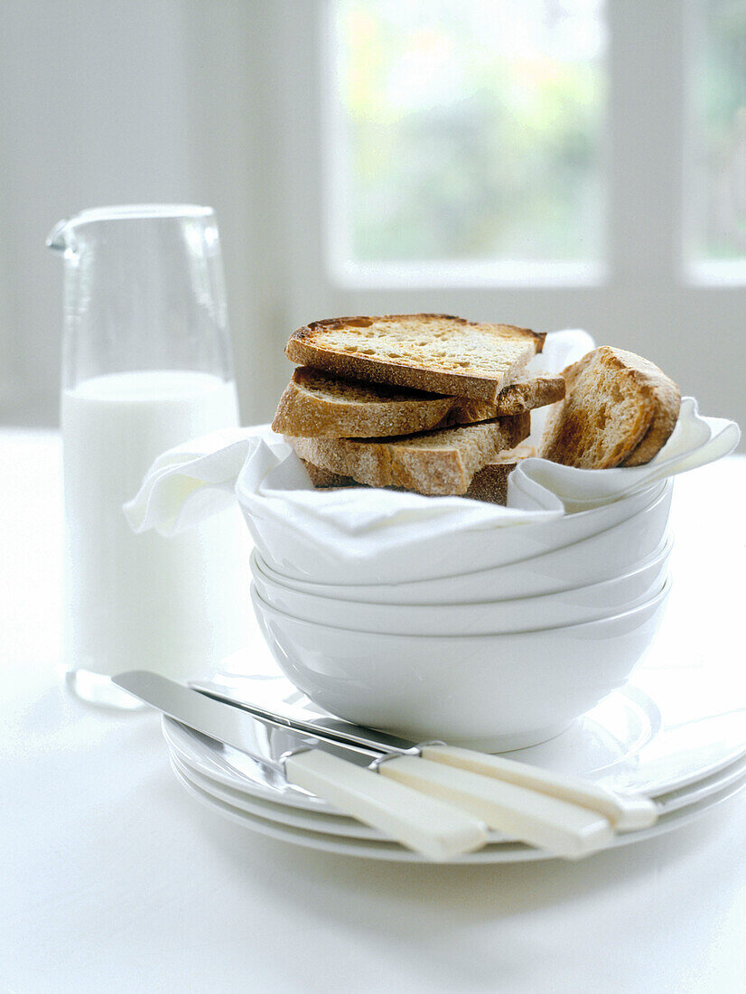 Frischer Toast und Milch mit Schüsseln und Messern auf dem Tisch