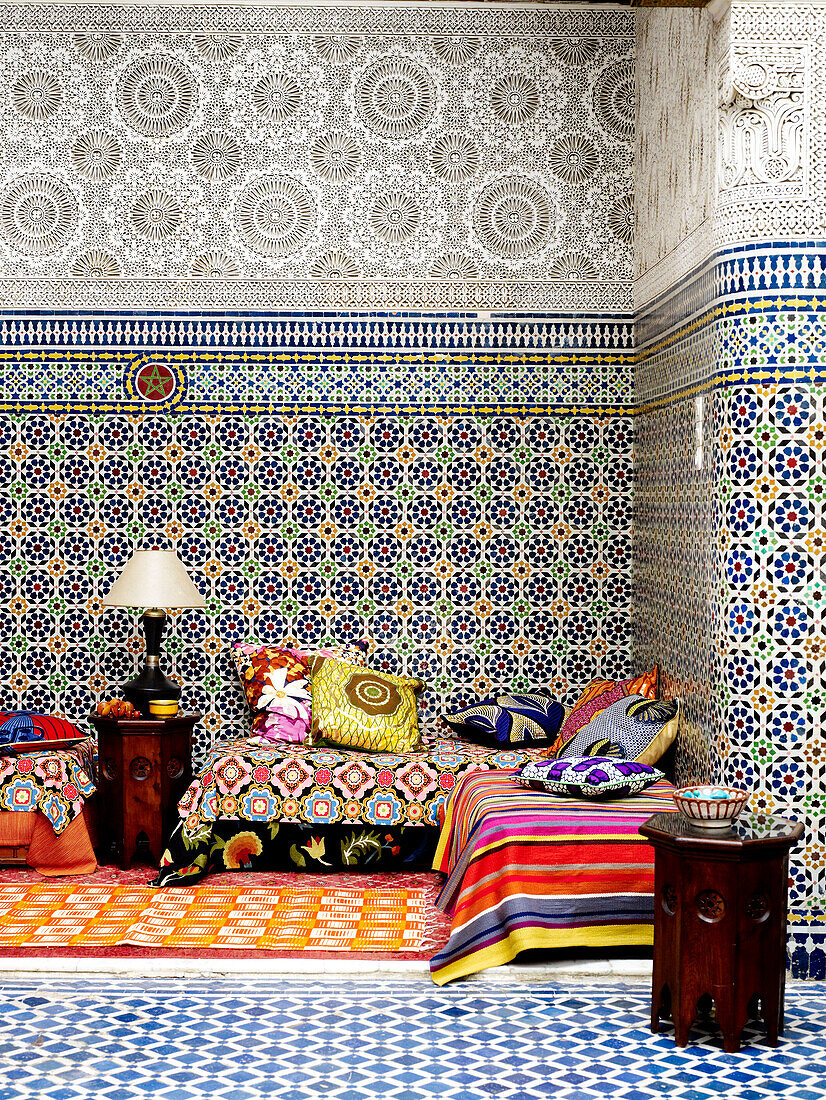 Bunte Stoffe auf einem Tagesbett in einem marokkanischen Riad mit geometrischen Kacheln in Nordafrika