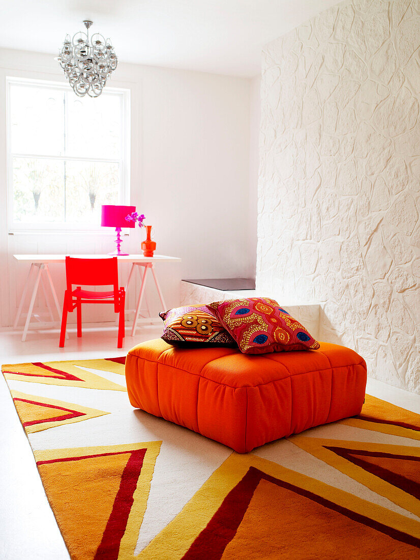 Bright cushions on ottoman with star patterned rug in whitewashed room