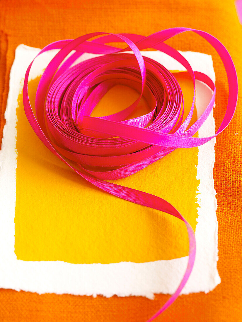 PInk ribbon on yellow painted paper with orange fabric