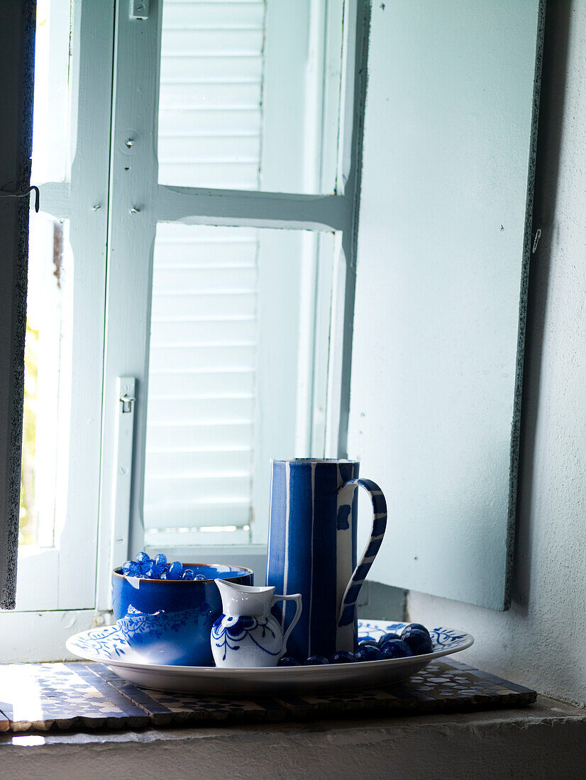 Blue and white chinaware on windowsill with light blue shutters Spain