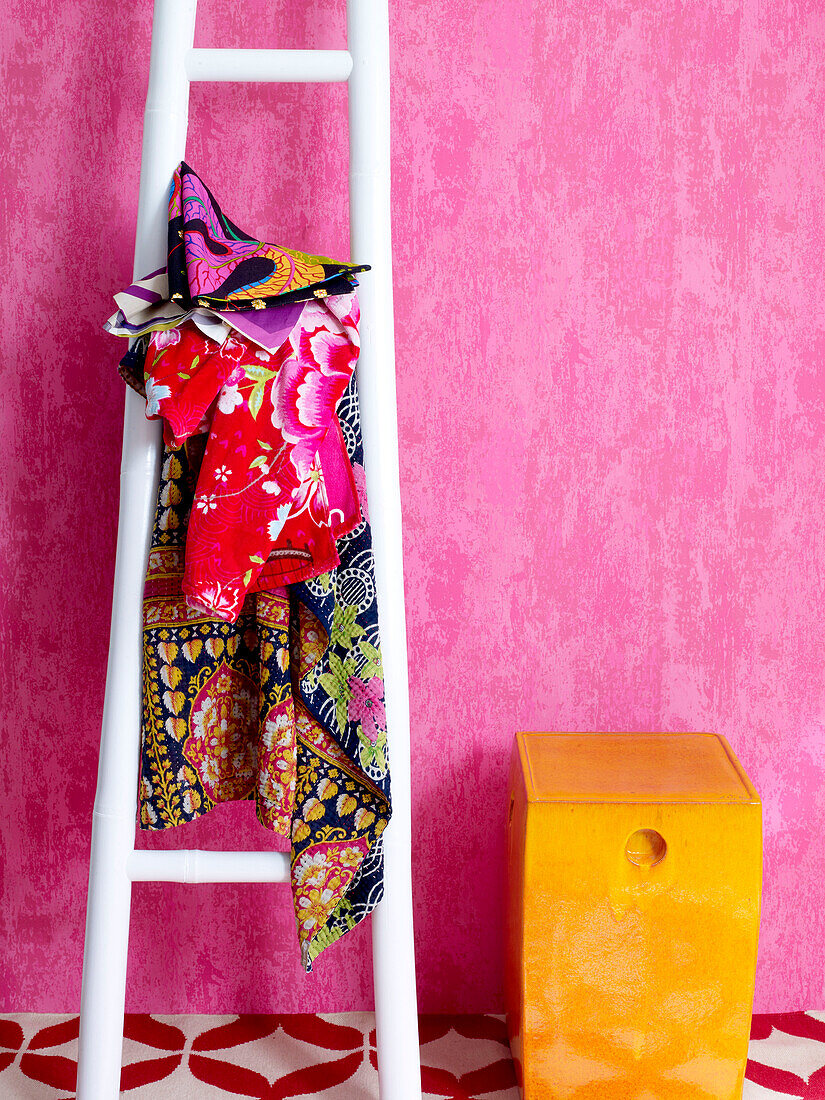 Bunte Stoffe auf einer Leiter vor einer rosa Wand