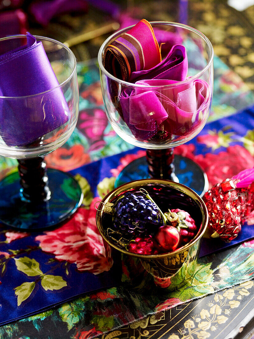 Assorted pink and purple ribbon in wineglasses with fruit baubles