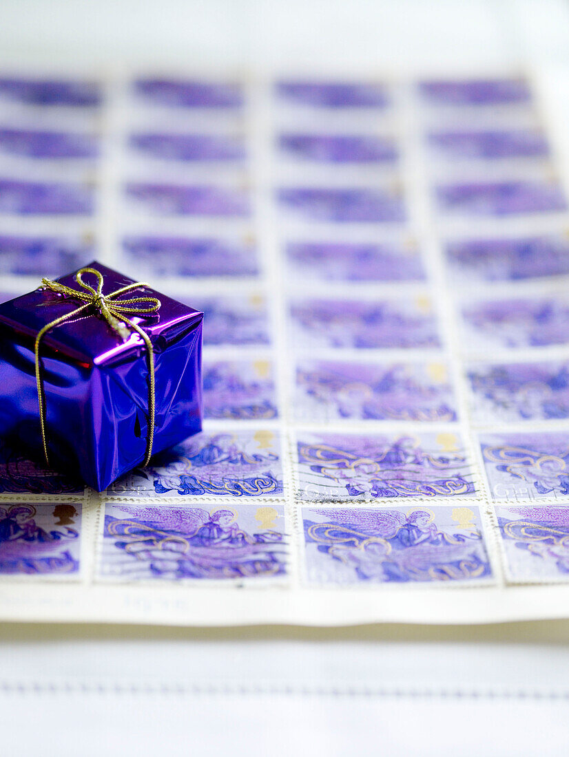 Tiny present wrapped with gold thread on sheet of postage stamps
