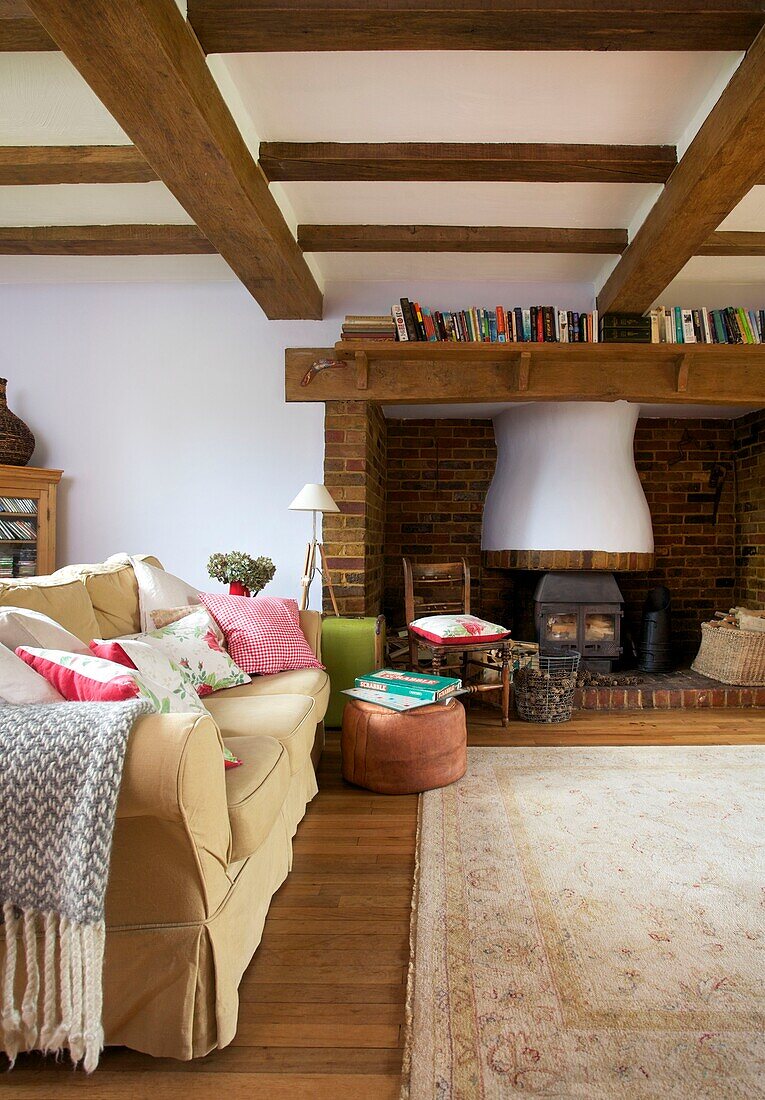 Bücherregal auf dem Kaminsims über dem Kamin mit cremefarbenem Sofa im Wohnzimmer eines Hauses der Familie Cranbrook, Kent, England, UK