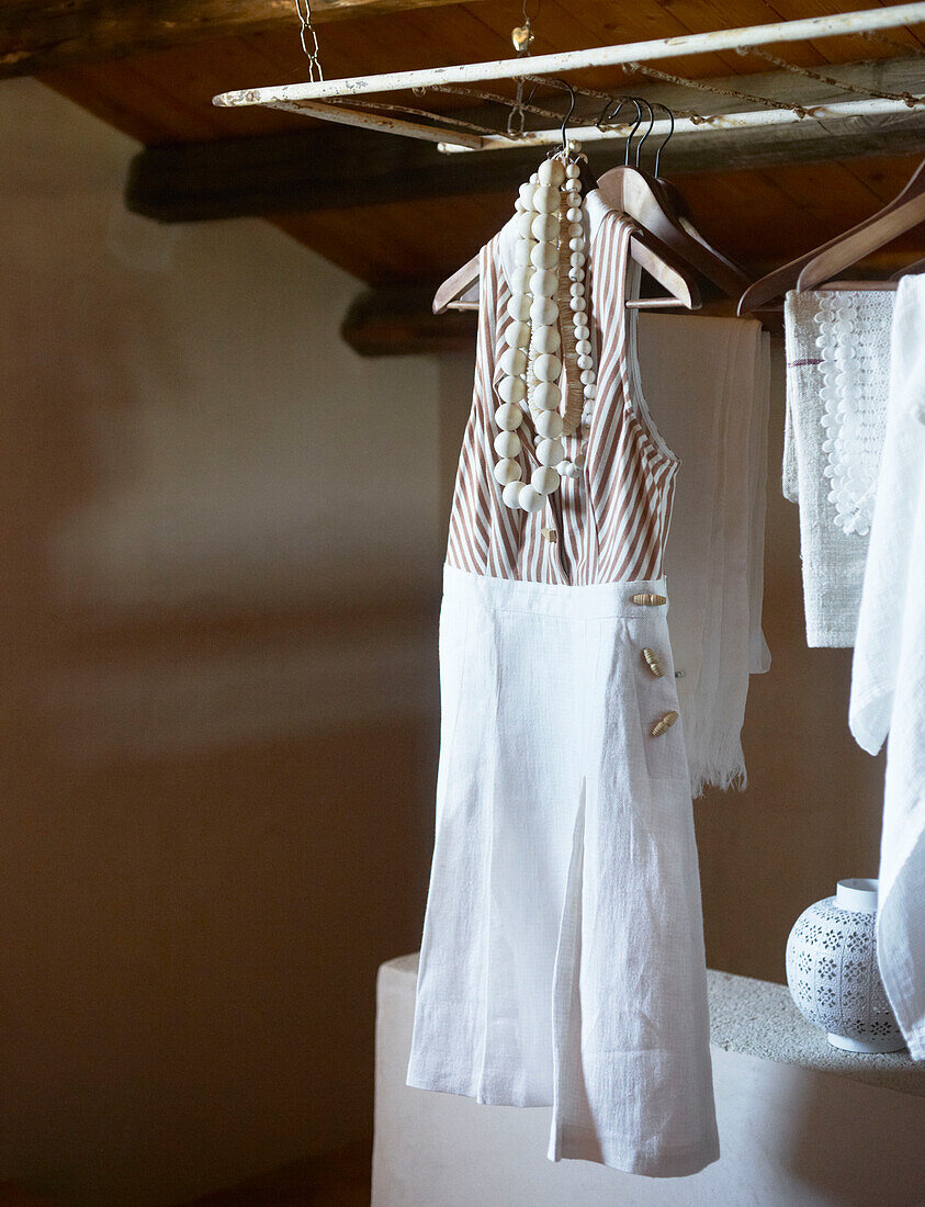 Sommerkleid und Halsketten auf einem Holzbügel in einem sizilianischen Haus