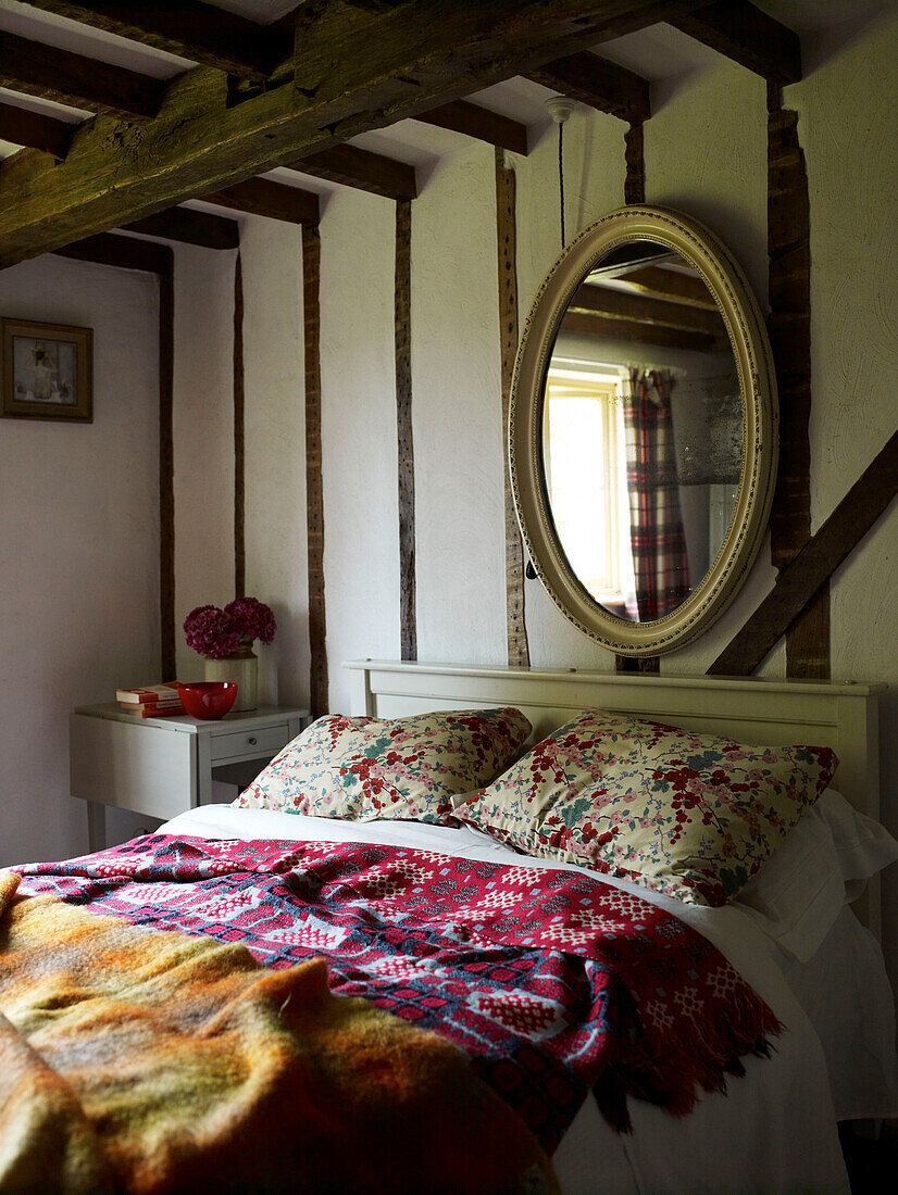 Großer Spiegel über dem Bett mit verschiedenen Bezügen in einem Bauernhaus mit Holzrahmen