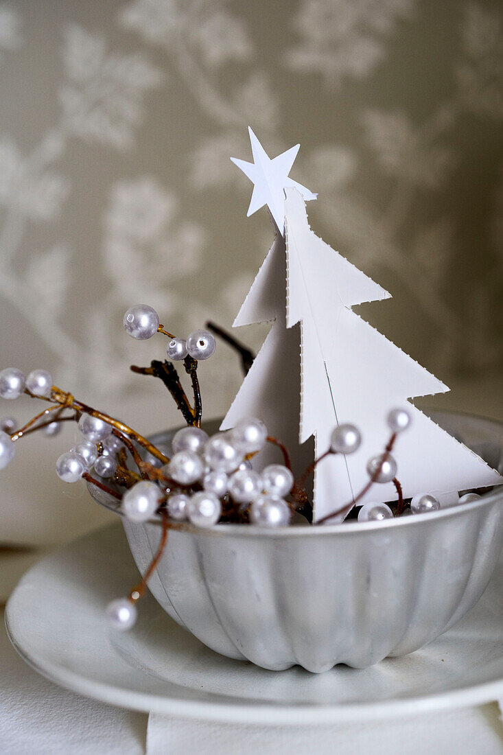 Weihnachtsbaum aus Karton mit Perlenbeeren in einer Metallschale