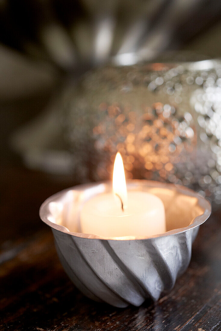 Single lit candle in metal bowl