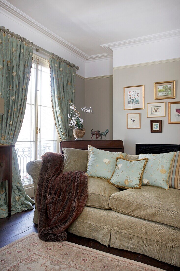 Pelzdecke auf dem Sofa mit Kunstwerken und grünen Seidenvorhängen in einem Haus in Cranbrook, Kent, England, UK