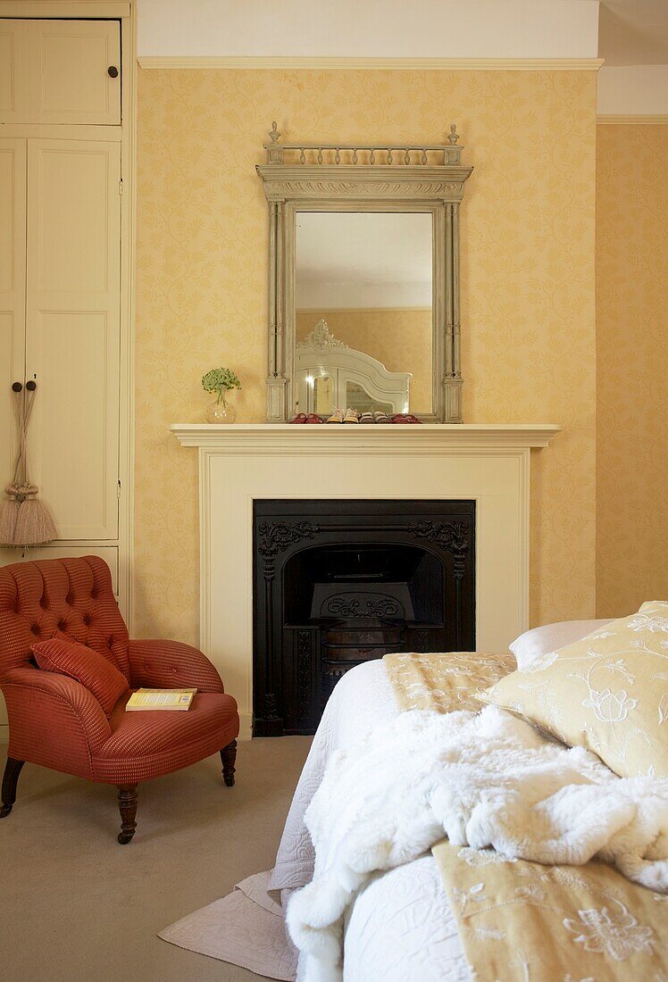 Armchair at fireplace with mirror in yellow bedroom of Cranbrook home, Kent, England, UK