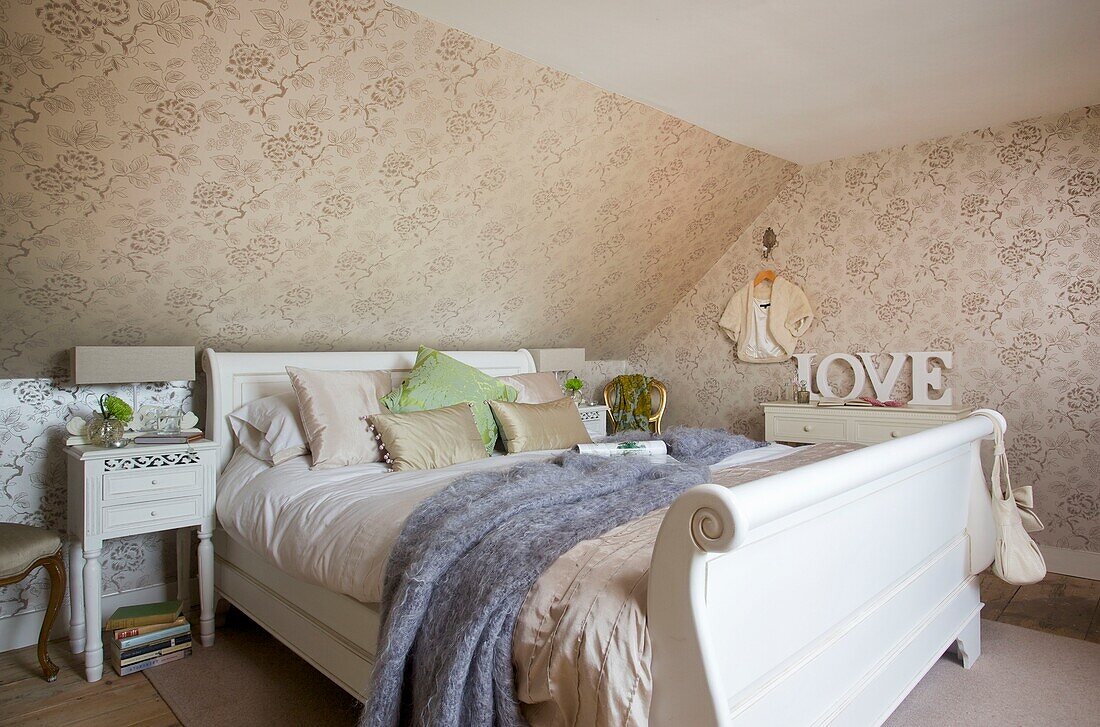 Painted white bed with blue blanket and floral wallpaper in bedroom of Cranbrook home, Kent, England, UK