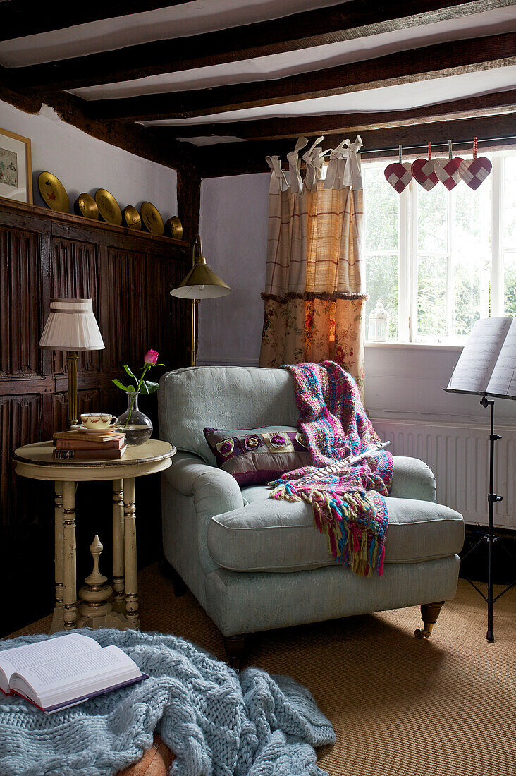 Sessel mit Decken und Notenständer in einer Ecke des Cottage in Sandhurst, Kent, England, UK