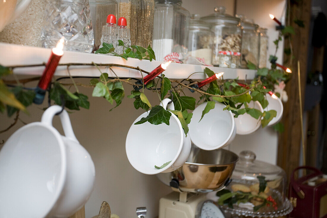 Teetassen hängen an einem Regal mit Oberlichtern in der Küche eines Hauses in Tenterden, Kent, England, UK