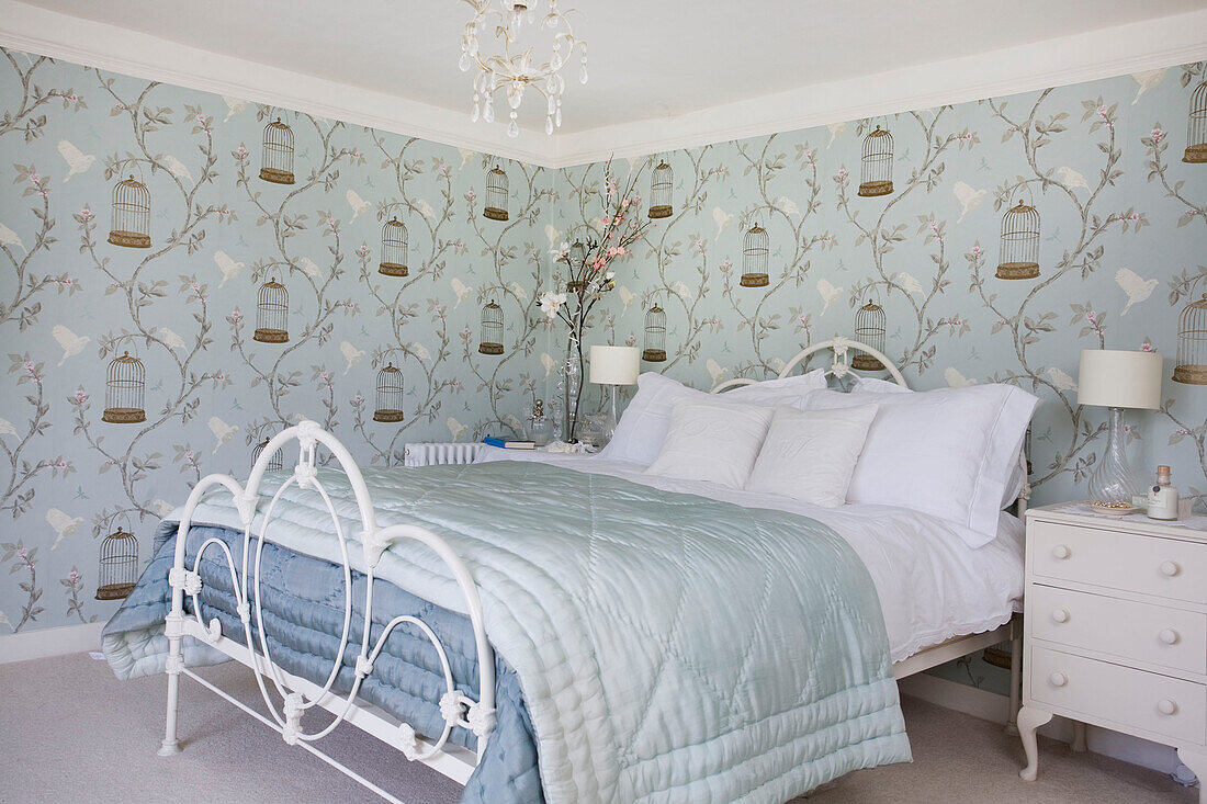 Hellgrüne und blaue Steppdecken auf einem Doppelbett in einem Zimmer mit Vogelkäfigmustertapete in einem Haus in Tenterden, Kent, England, UK
