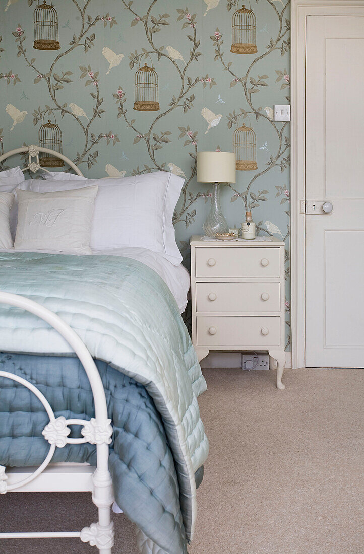Hellgrüne und blaue Steppdecken auf dem Bett in einem Zimmer mit Vogel- und Vogelkäfigmustertapete in einem Haus in Tenterden, Kent, England, UK