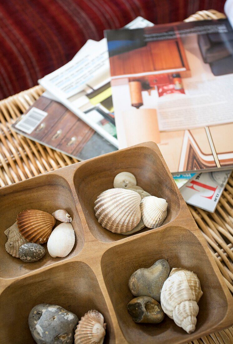 Muscheln und Zeitschriften auf einem Korb im Haus einer Familie in Tenterden, Kent, England, UK