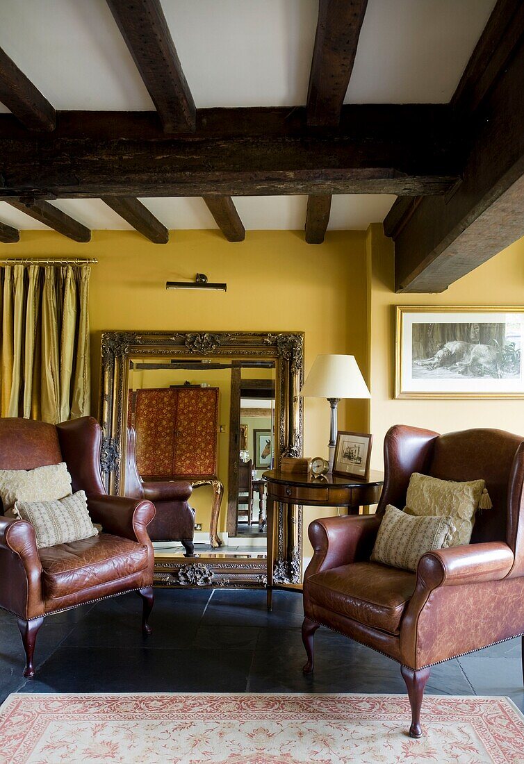 Brown leather armchairs and gilt mirror in timber framed cottage, Grafty Green, Kent, England, UK