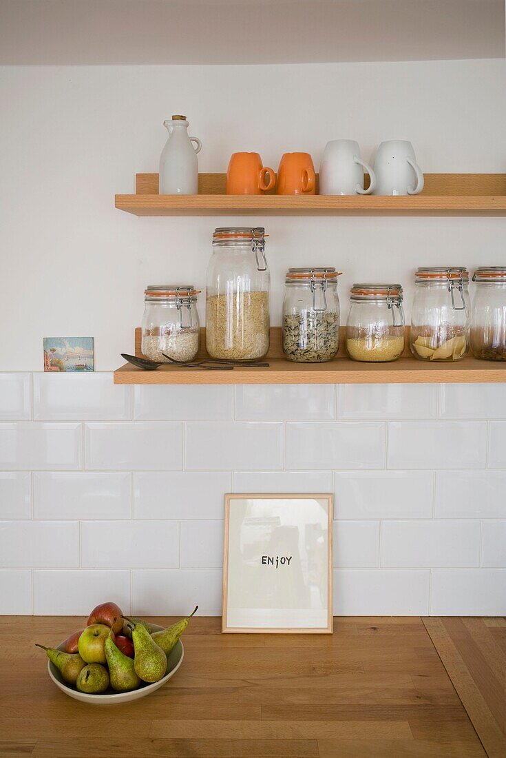 "Vorratsgläser und eine Schale mit Birnen mit dem Schriftzug Enjoy"" auf einer hölzernen Küchenarbeitsfläche in einem Haus in St Leonards, East Sussex, England, UK"""