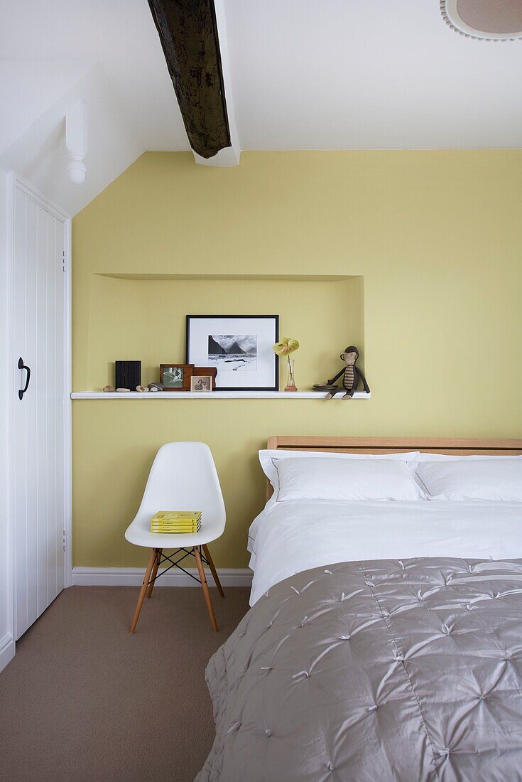 Einzelbett mit grauer Bettdecke in einem gelben Schlafzimmer in einem Cottage mit Holzrahmen