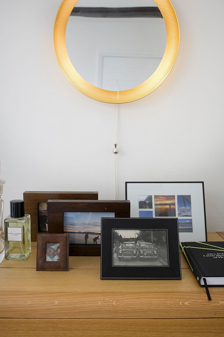 Family photographs and books on wooden sideboard below circular mirror