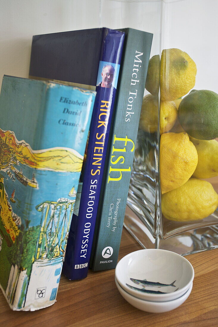 Zitronen und Limetten in einer Glasvase mit Büchern über die Zubereitung von Meeresfrüchten in einem Haus in Dartmouth, Devon, Vereinigtes Königreich