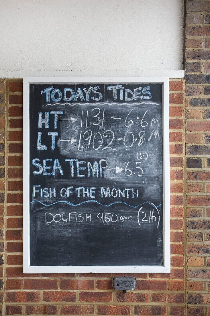 Gezeitenzeiten auf einer Tafel an einer Backsteinmauer in Deal Kent England UK