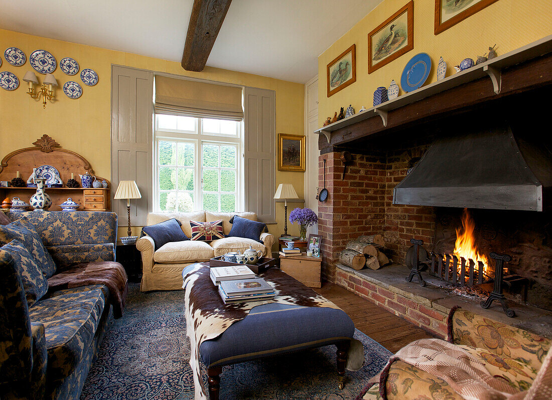 Sofas at lit fireside in living room of Etchingham farmhouse East Sussex England UK