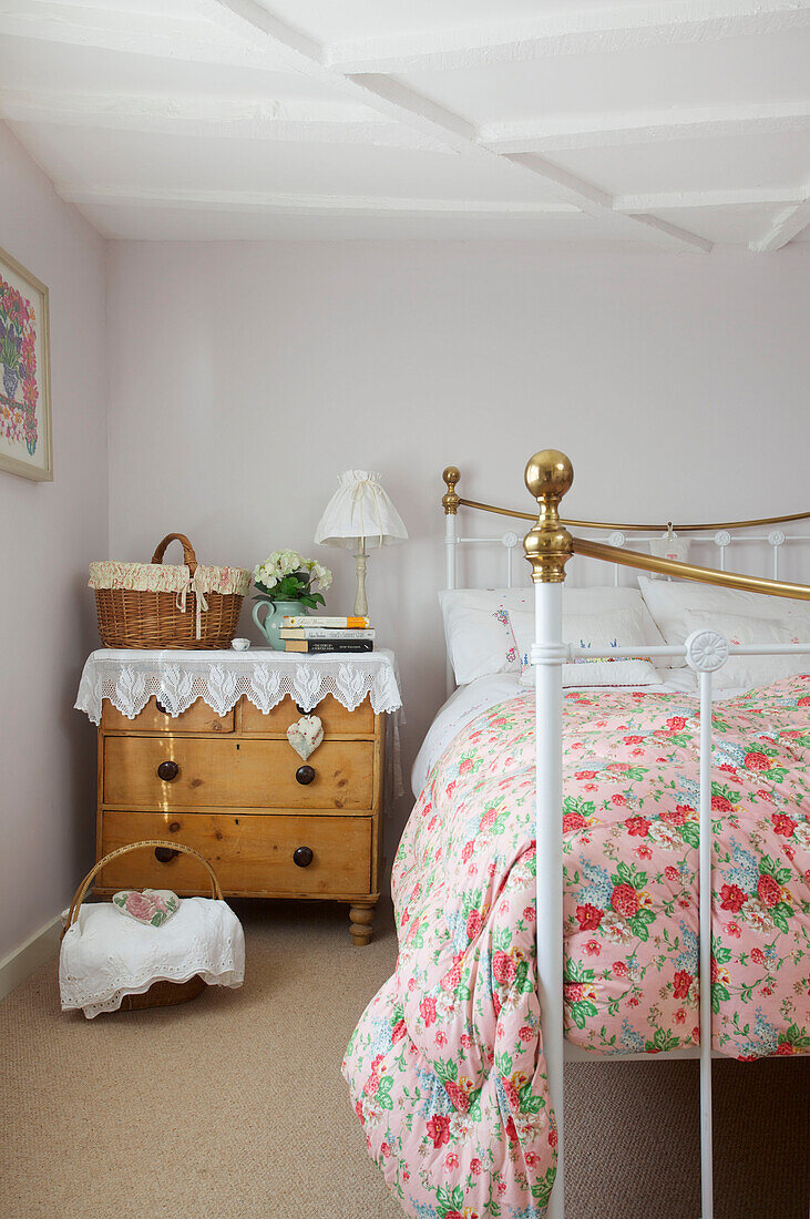 Floral quilt on brass bed with wooden chest of drawers in High Halden farmhouse Kent England UK