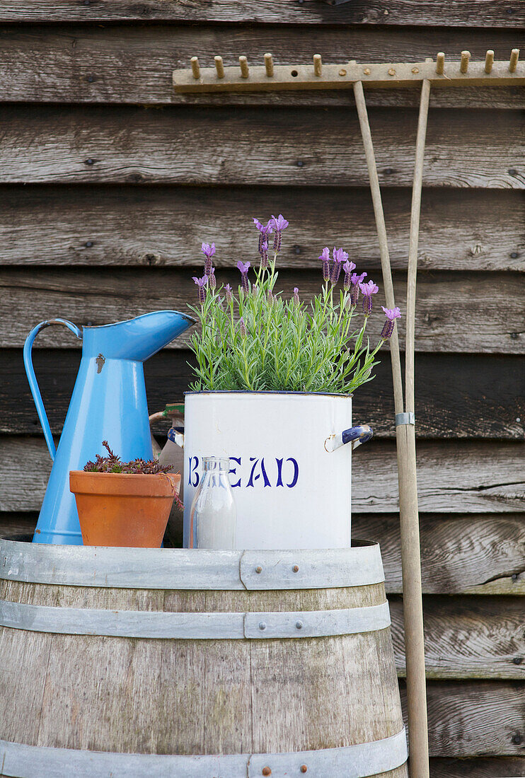 Metallkrug und Blumen auf Fass mit Gartengabel im Garten von High Halden, Kent, England, UK