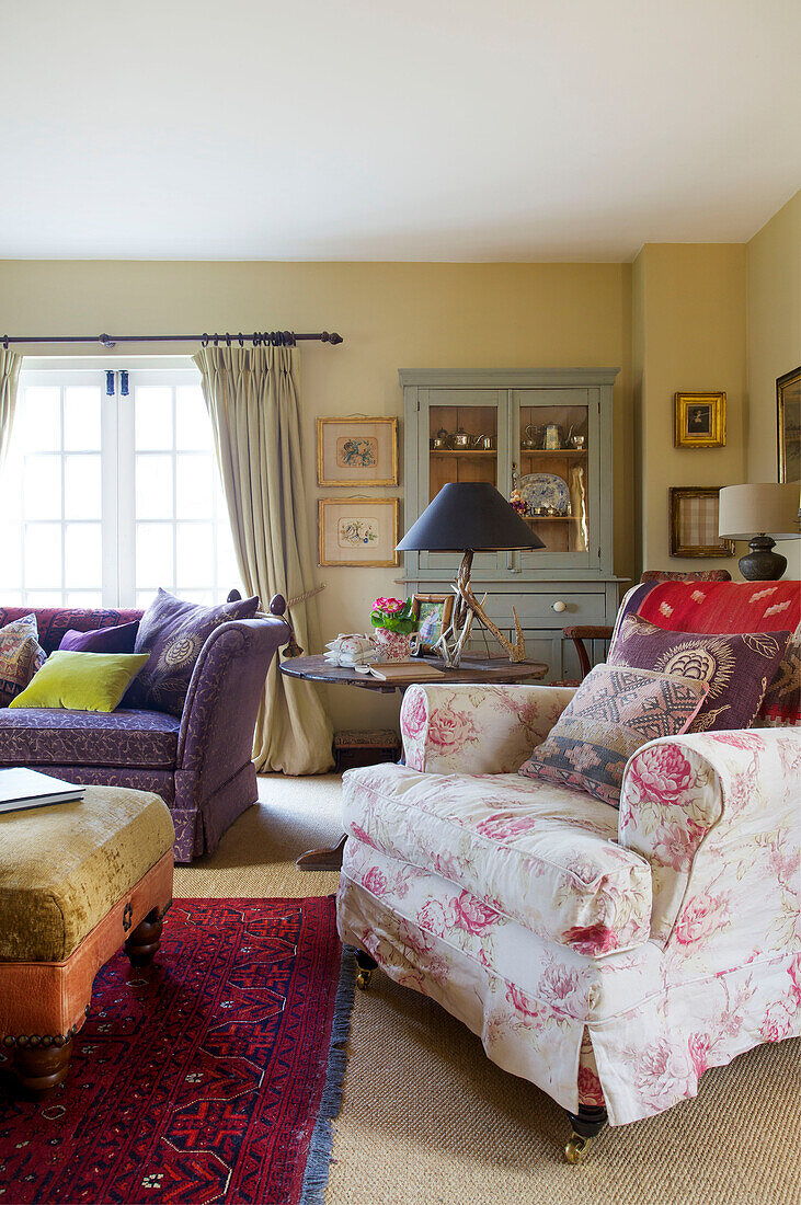 Sessel mit Blumenmuster und lilafarbenes Sofa mit Ottomane im Wohnzimmer eines Bauernhauses in Kent, England, UK