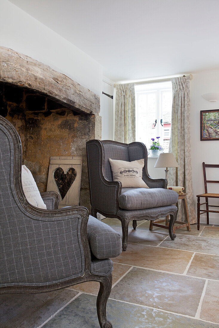 Pair of grey upholstered armchairs with carved heart at fireplace in Dorset cottage Corfe Castle England UK