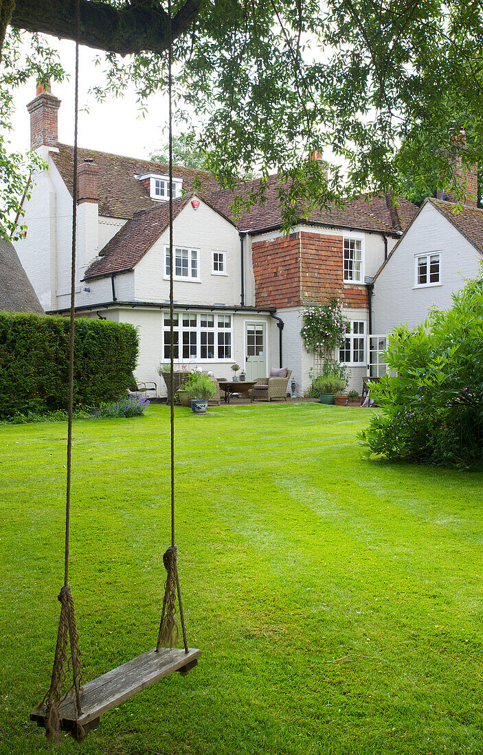 Rope swing in lawned garden exterior of whitewashed Bishops Sutton detached house Alresford Hampshire England UK