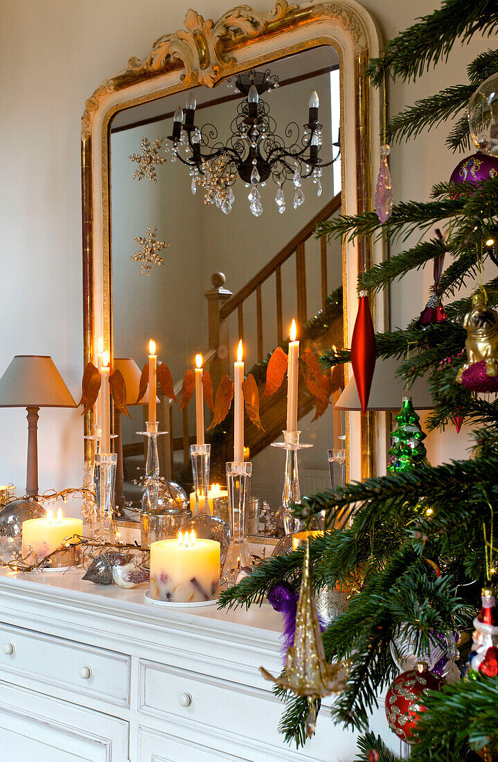 Lit candles on white sideboard with Christmas tree in hallway of Faversham home Kent England UK