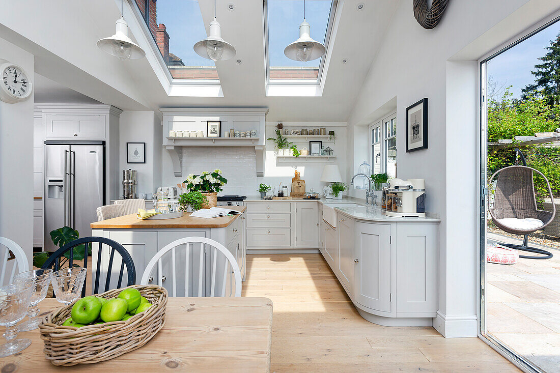 Pale grey open plan kitchen diner with three skylights and pendant lights and bi-fold doors on to the garden Oxfordshire UK