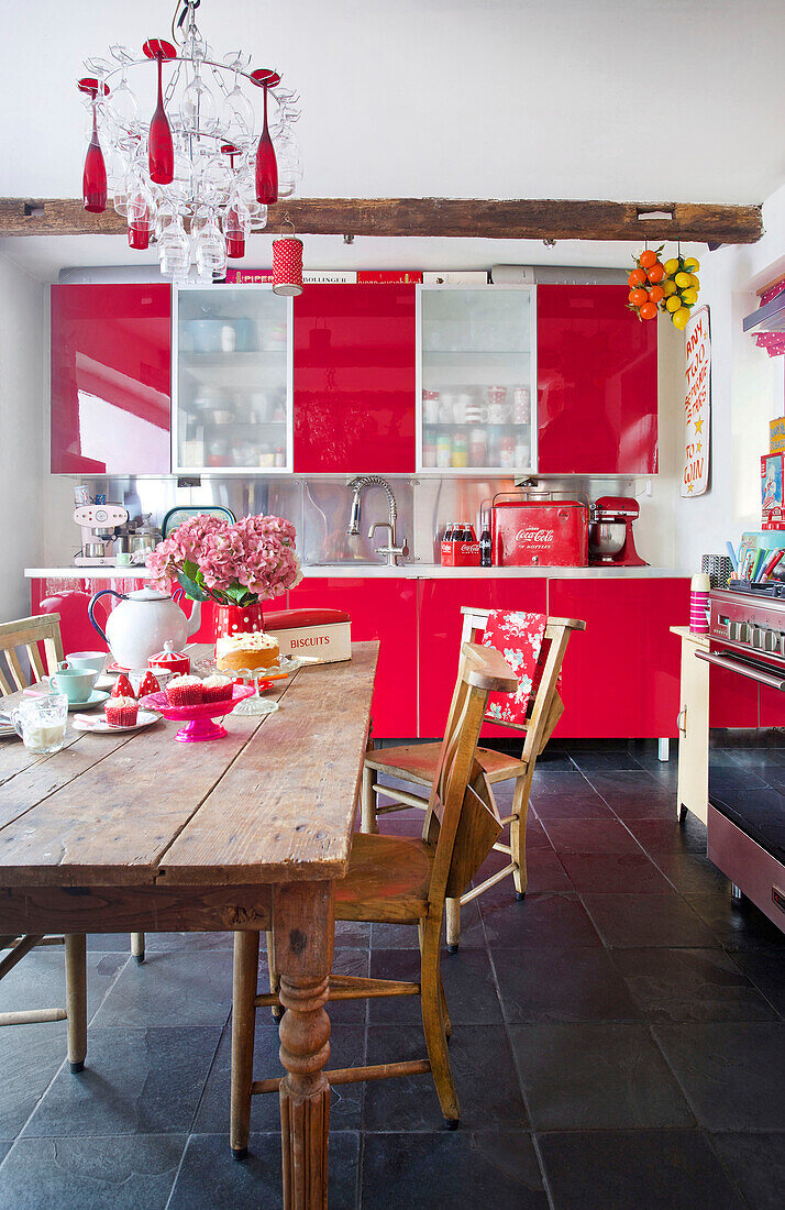 Leuchtend rote Schränke mit Holztisch in einer Küche in Tenterden, Kent, Großbritannien