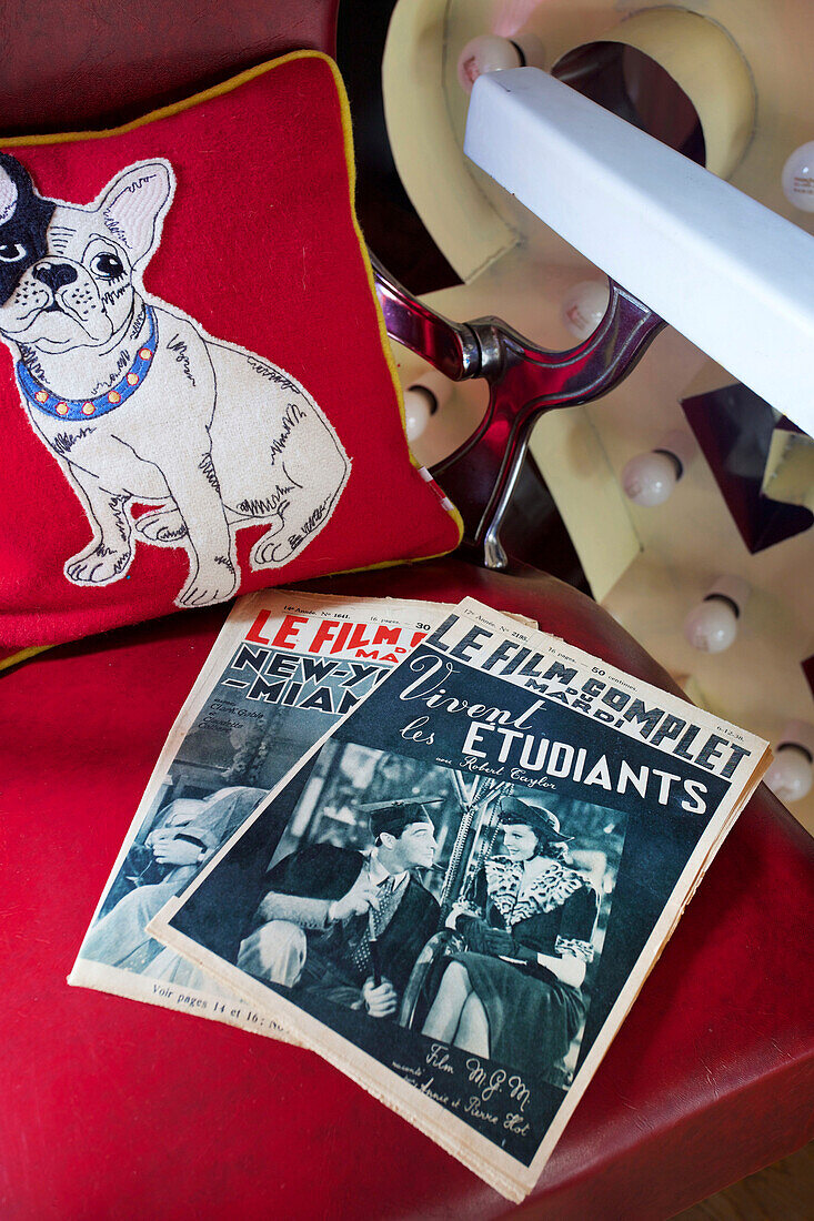 Französische Zeitschriften im Vintage-Stil mit Bulldoggenkissen auf einem Stuhl in einem Haus in Tenterden, Kent, Großbritannien