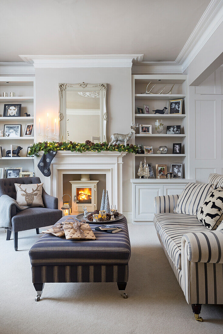 Striped sofa and ottoman with lit woodburner and Christmas decorations in London home UK
