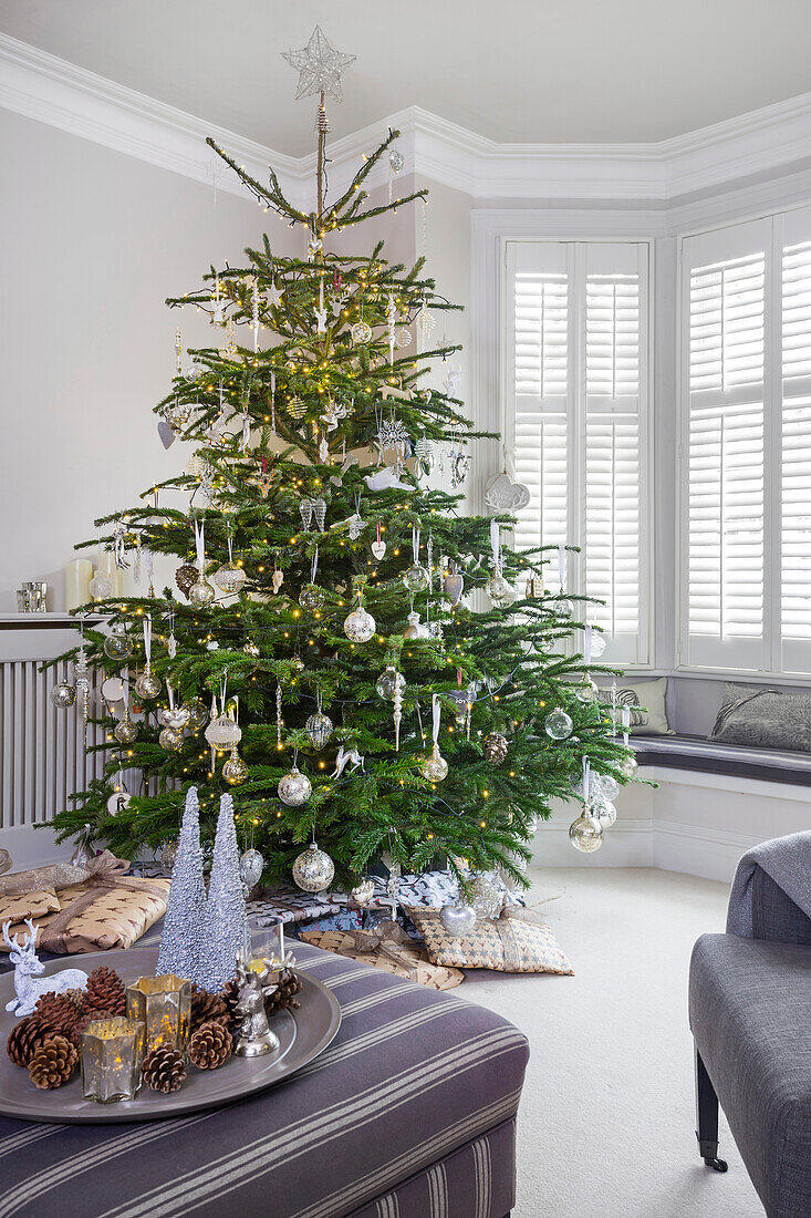 Weihnachtsbaum mit Glaskugeln und gestreifter Ottomane in einem Haus in London UK